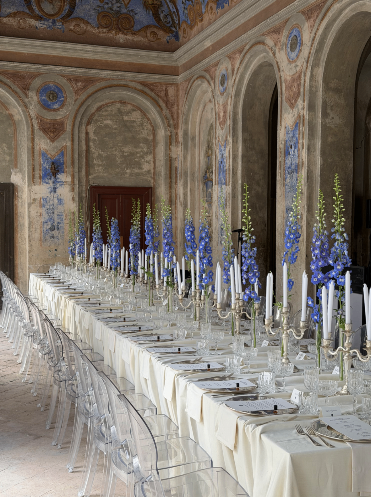 Tavolata cerimoniale con candelabri e delphinium blu sotto gli affreschi